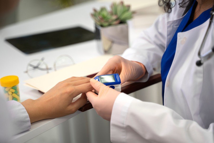 Doctor using a fingertip blood glucose monitor to check a patient's blood sugar during a diabetes consultation in North Delhi.