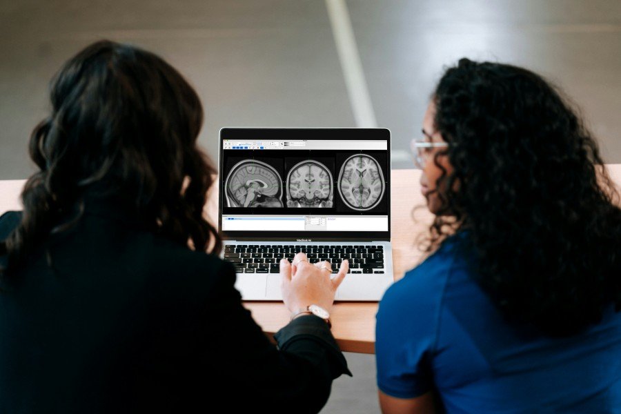 Two women looking at brain MRI scans displayed on a laptop.