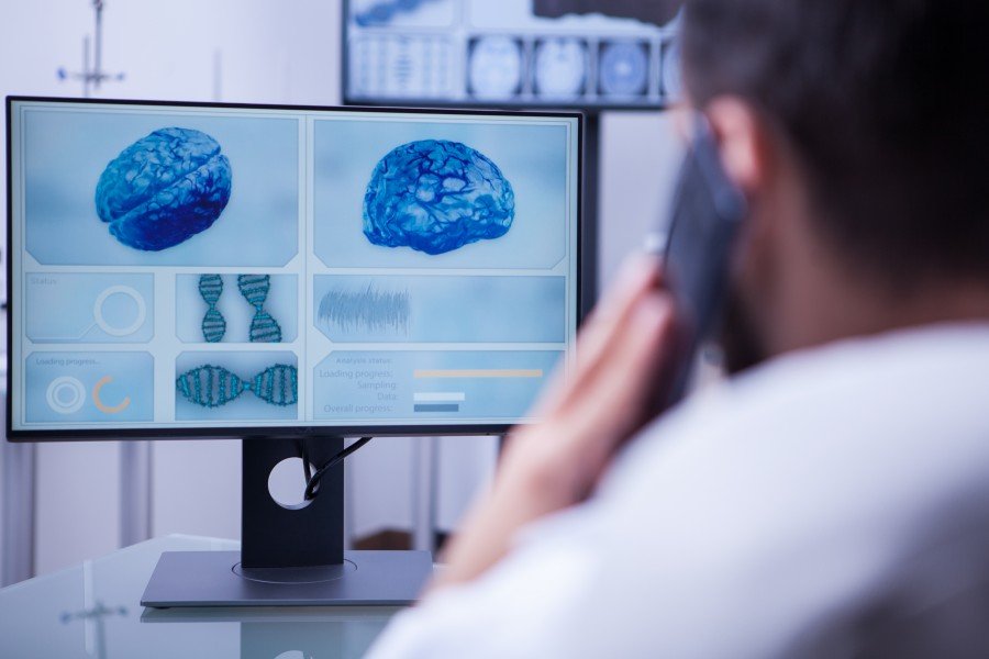 Neurotherapist examining brain scans on a computer while talking on a smartphone
